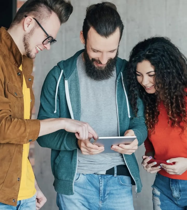 Lifestyle photo of three young adults looking down at a mobile device together, representing peer collaboration, shared learning, and community connection.