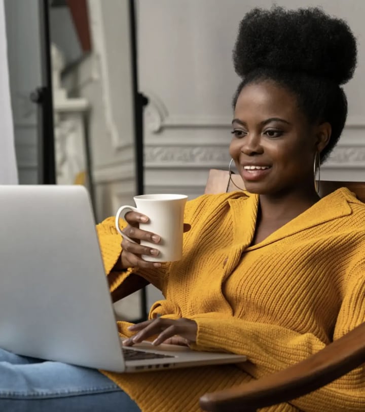 Smiling Black woman sitting with a laptop and coffee mug, representing digitally connected next-gen investors engaging with online content.